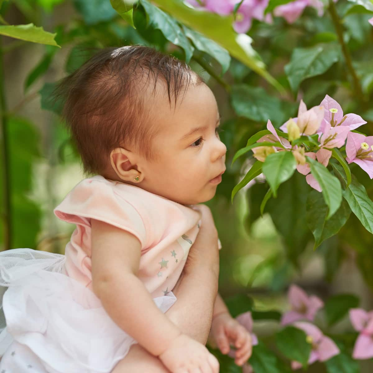 Baby being held next to flowers.