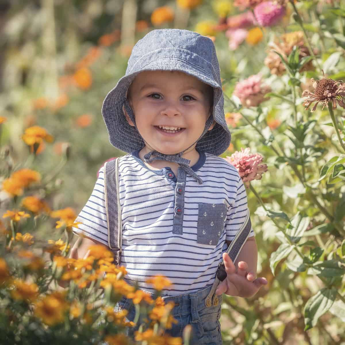 Toddler standing in a garden with hat on.