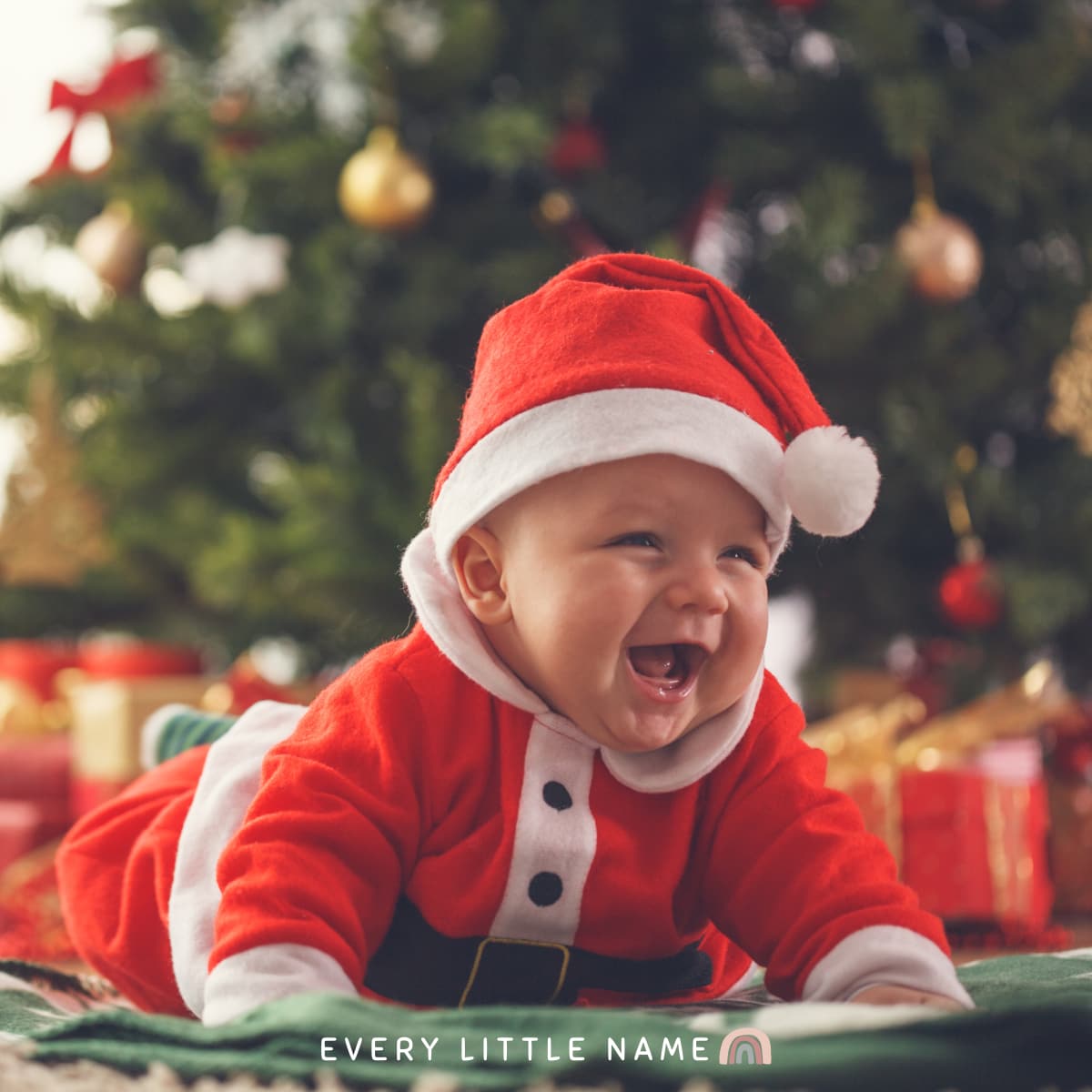 Laughing baby crawling in Santa outfit.